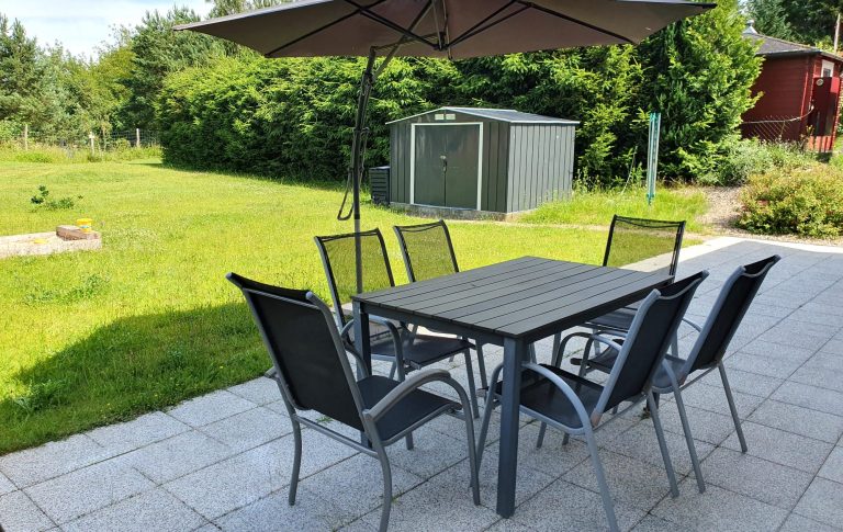 Terrasse mit Tisch, Stühlen und Sonnenschirm. Im Hintergrund steht das Gartenhaus.