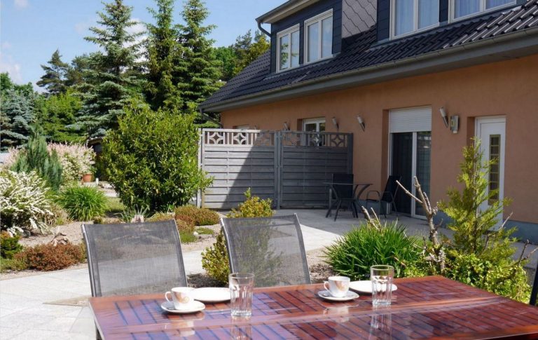 Gedeckter Tisch auf der Terrasse. Im Hintergrund ist unser Ferienhaus und der Vorgarten zu sehen.